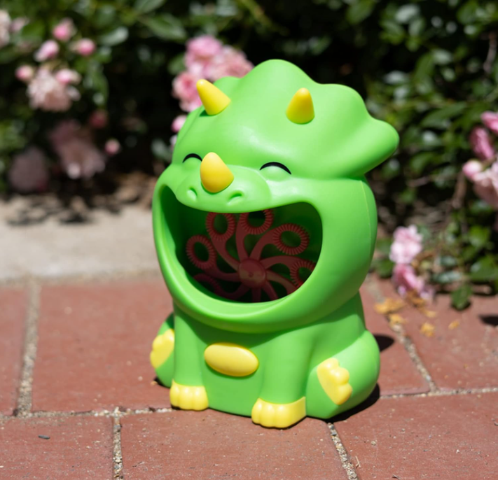 Green dinosaur-shaped container with a red interior on a brick surface with flowers in the background